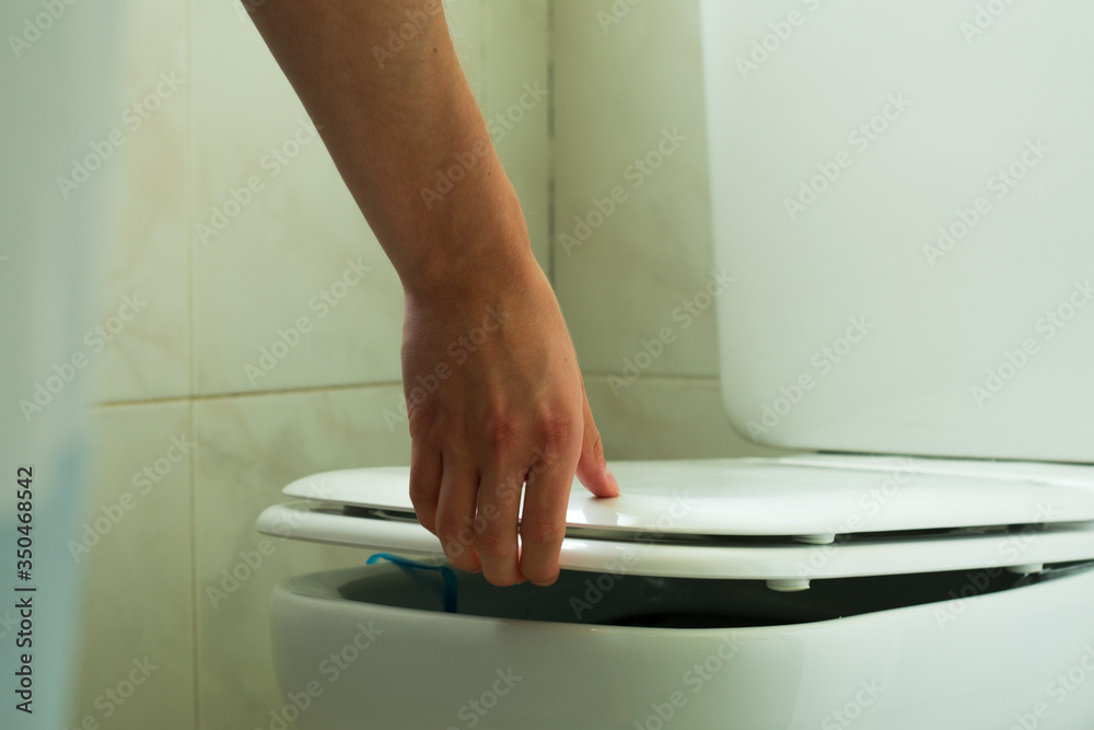 Fototapeta premium Mano levantando la tapa del baño en un cuarto blanco. 