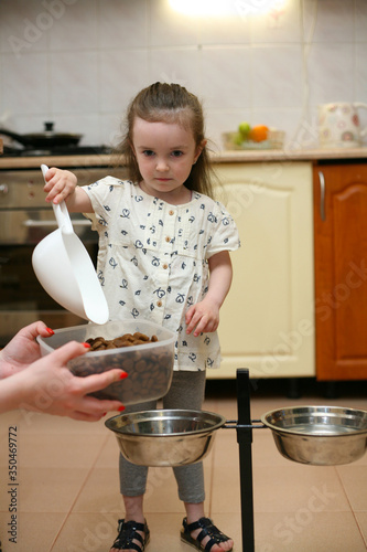Dog is a friend of man. A little girl pours food into a bowl for her dog. Pet. Pours feed with a white plastic spatula.
