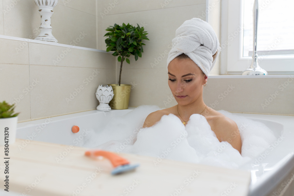 Junge Frau in der Badewanne mit viel Schaum Handtuch auf dem Kopf, Rasierer, rasiert sich die