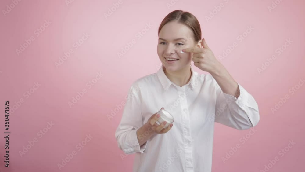 A beautiful young girl applies white cream on her face with one strip. A beautiful young girl applies white cream on her face with one strip.