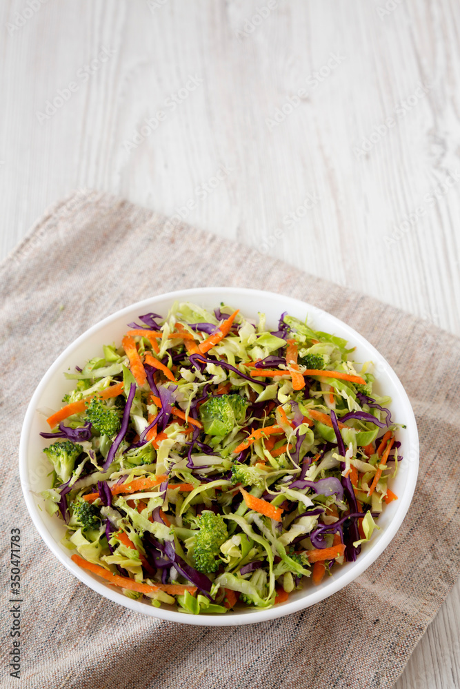 Homemade Raw Shredded Broccoli Slaw in a white bowl on a white wooden surface, side view. Copy space. Homemade Raw Shredded Broccoli Slaw in a white bowl on a white wooden surface, side view. Copy space.
