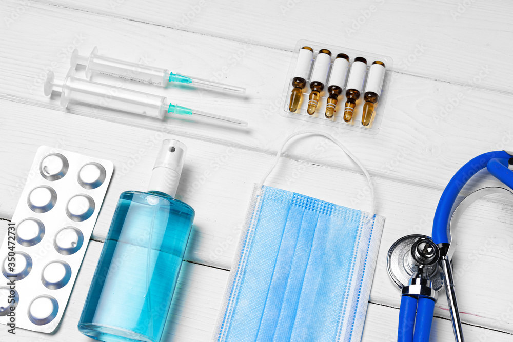 Medical equipment. Stethoscope, mask and pills on white wooden desk close up Medical equipment. Stethoscope, mask and pills on white wooden desk close up