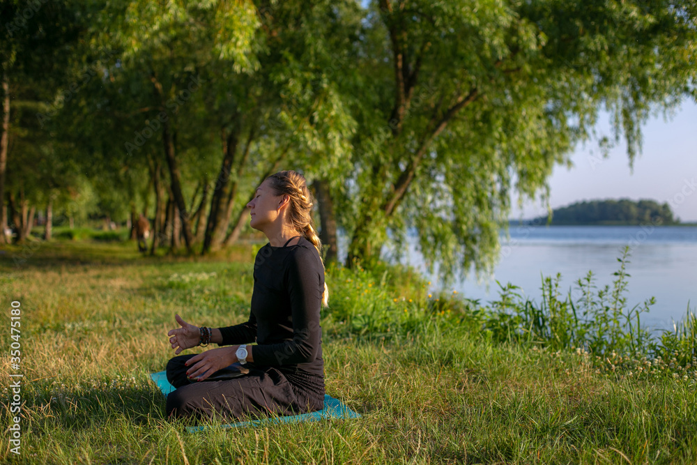 horizontal photo of a young woman doing yoga in a beautiful summer park by the river