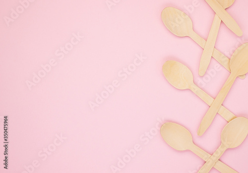 Eco-friendly biodegradable compostable wooden spoons on a soft pink background. Wooden spoons are gathered together on the right side. Background for the holidays