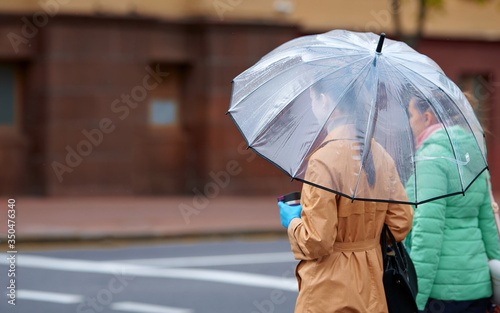 Couple with transparent umbrella walking along the street in rainy day. Womens under transparent umbrella in rainy weather standing next to a pedestrian crossing