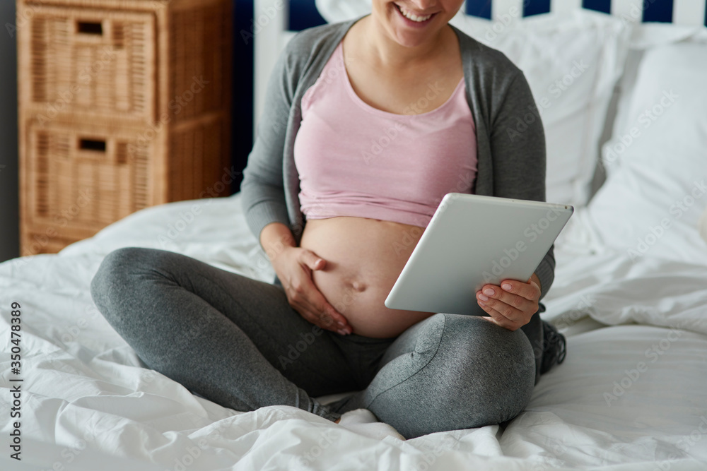 Unrecognizable pregnant woman using tablet in bed Unrecognizable pregnant woman using tablet in bed