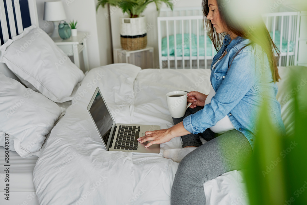 Pregnant woman sitting on bed and using a computer Pregnant woman sitting on bed and using a computer