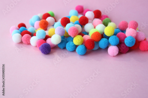 A lot of bright fur pompons on a pink background. Concept - needlework, decor, handmade. There is a place for text.