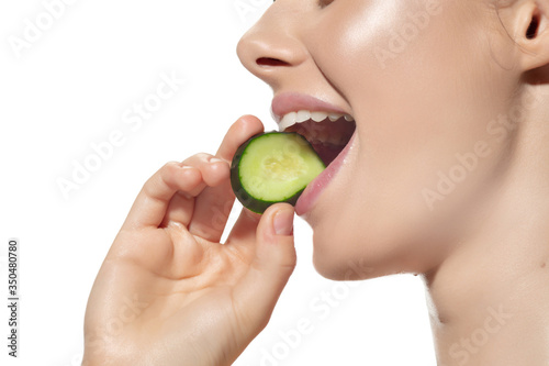Close up of beautiful young woman with cucumber's slice over white background. Concept of cosmetics, makeup, natural and eco treatment, skin care. Shiny and healthy skin, fashion, healthcare.
