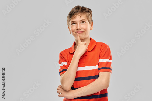 childhood, fashion and people concept - portrait of happy thinking boy in red polo t-shirt over grey background