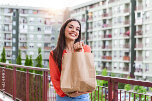 Woman Doing Shopping For Senior Neighbors. Young beautiful woman holding take away paper bag from delivery