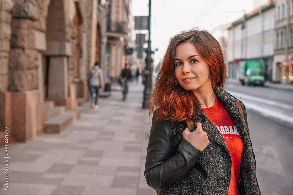 A young girl in a jacket walks through the streets of the city, portrait against the background of a beautiful old building, business style