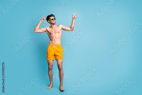 Full length body size photo of cheerful positive man with stubble dancing with forefingers up in sunglass eye wear yellow shorts isolated pastel color background