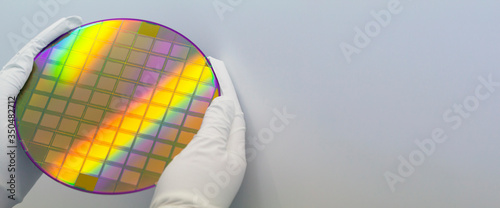 Hands in white gloves holding a silicon wafer with microchips on white background.Banner format.