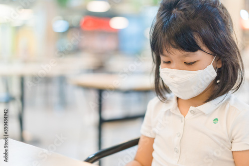 Asian kid girl in canteen at school.Student girl wearing fabric face mask sitting distancing in restaurant in shopping mall.Social distancing concept.Partition board for separated in restaurant.People