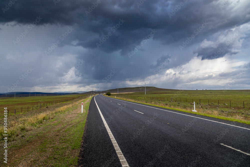 A lonesome road leading through the Kosciuszko national park in the Snowy Mountains, a part of the Australian alps, during a cloudy day in summer.