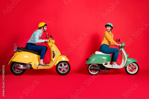 Profile side view of her she his he nice attractive positive cheerful cheery couple riding moped having fun time fast speed racing isolated on bright vivid shine vibrant red color background