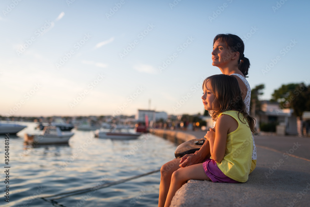 Fototapeta premium Daughter sitting along with loving mother near the sea