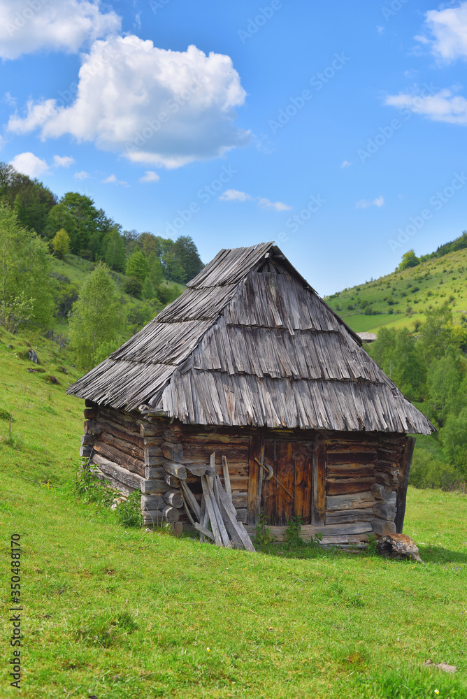 Lonely old wood house on a mountain hill with green grass against blue sky