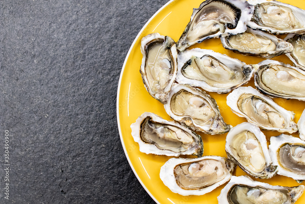 Fresh oysters ready to be eaten raw. Oysters on a yellow plate and a black stone. Raw fish with oysters, luxurious dinner and quality fresh shellfish. Restaurant special dish Fresh oysters ready to be eaten raw. Oysters on a yellow plate and a black stone. Raw fish with oysters, luxurious dinner and quality fresh shellfish. Restaurant special dish