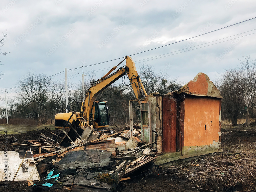 Excavator destroying brick house on land in countryside. Bulldozer clearing land from old bricks and concrete from walls with dirt and trash. Backhoe machinery ruining house Excavator destroying brick house on land in countryside. Bulldozer clearing land from old bricks and concrete from walls with dirt and trash. Backhoe machinery ruining house
