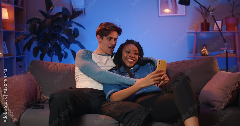 Millennial happy couple making funny selfies while sitting on sofa. Handsome guy and his attractive african girlfriend with dreadlocks posing while making photos and spending time at home Millennial happy couple making funny selfies while sitting on sofa. Handsome guy and his attractive african girlfriend with dreadlocks posing while making photos and spending time at home