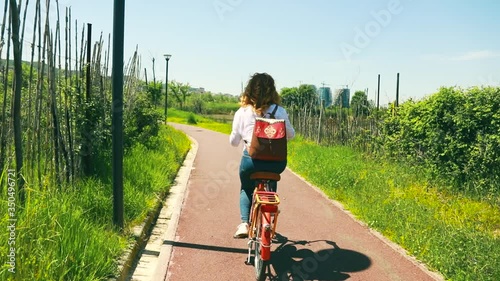 Female taking a ride with bicycle on quiet path of city park surrounded by green vegetation photo