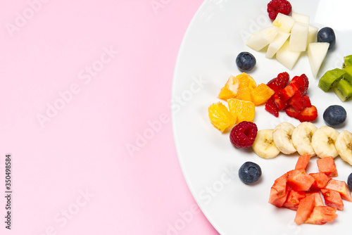 Fresh fruit salad on white plate. Mixed fruit in white plate healthy food style. Useful fruit salad of fresh fruits and berries on pink background