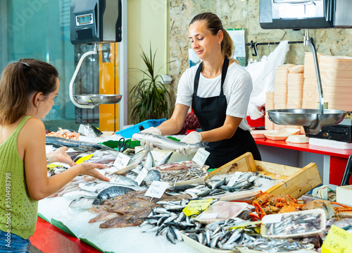 Confident worker offering fresh sea bass to woman