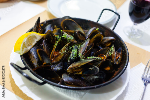 Delicious mussels on a frying pan with lemon at table