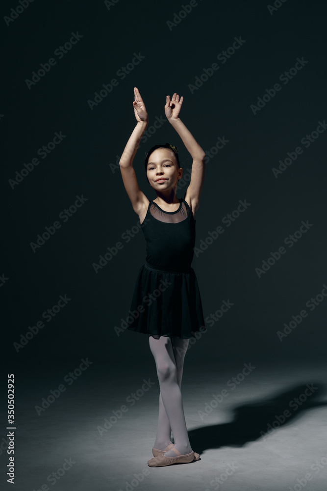 Beautiful girl ballerina dancing in light play and shadowson dark background