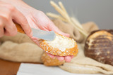 Rustic breakfast cooking. Hands of woman spreading butter onto slice of baguette with knife. Closeup shot. Traditional bread or eating concept