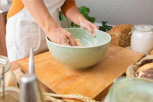 Skilled cook in apron kneading dough for delicious pastry and bread. Ingredients in glass jars standing around. Fresh cereal loaf. Studio shot. Side view. Homemade food and nutrition concept