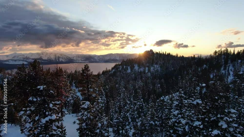 A cinematic drone movement flying forward past snowy trees to reveal a beautiful sunset over Lake Tahoe in California during golden hour showing the beauty of nature of winter at this alpine lake. A cinematic drone movement flying forward past snowy trees to reveal a beautiful sunset over Lake Tahoe in California during golden hour showing the beauty of nature of winter at this alpine lake.
