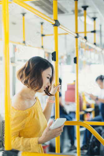 Attractive young Asian woman using phone when standing on the bus.