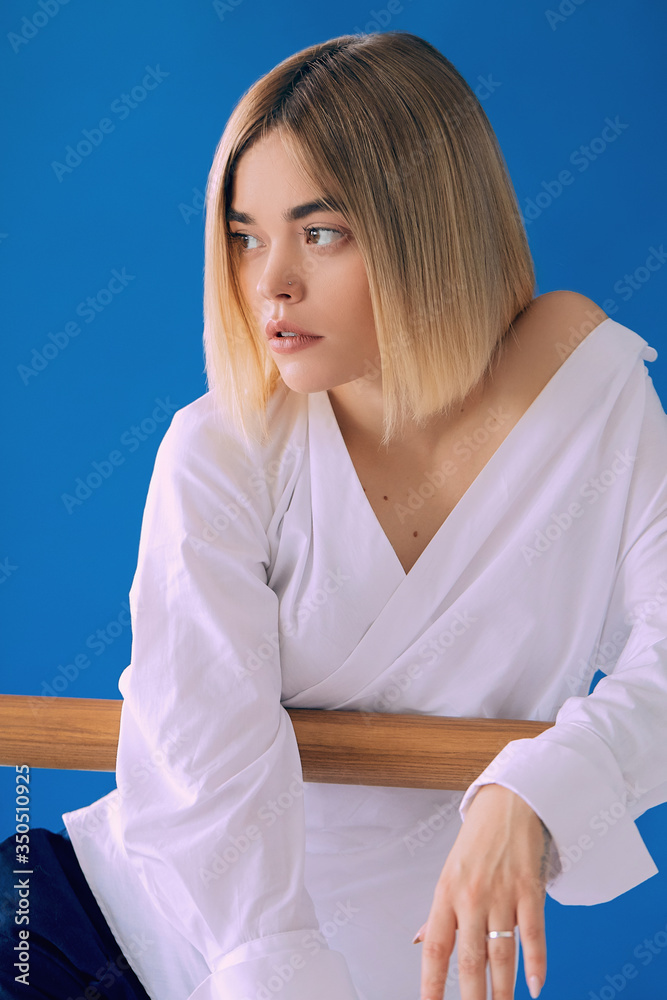 Fototapeta premium Portrait of a pretty blonde woman in white shirt posing with wood stick