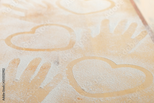 Heart and hand prints and drawing with flour on the board. Rough wooden rectangular used cutting board background with flour top view. Kitchen equipment. Concept of baking homemade, pastry copy space