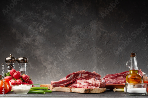 Photos Fresh pork ribs on a background of vegetables, with empty space on a gray background