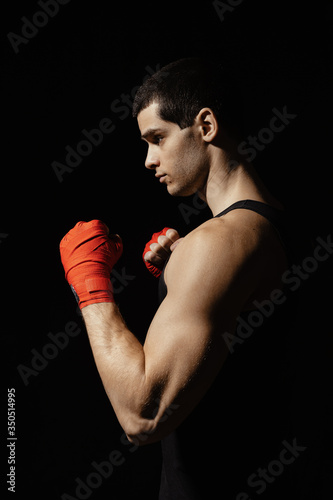 Sportsman boxer practicing side kick. Red bandages on the hands. Muscular boxer on black background. Sport concept.