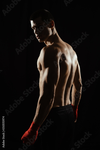 Portrait of male boxer posing in boxing stance, looking over shoulder, against black background. © arthurhidden