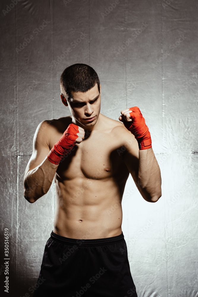 Boxing male portrait standing in a rack on black background with red bandages on his hands. Light and shadows play.