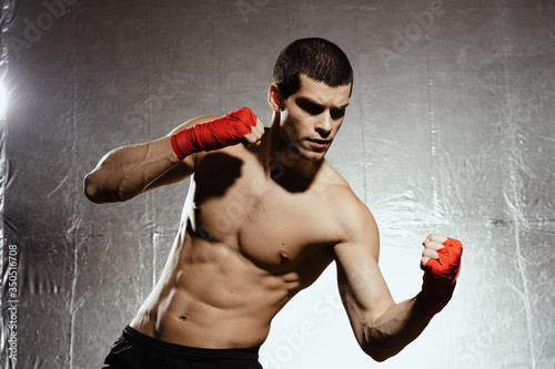 Uppercut punch. Confident handsome athlete with naked torso throwing uppercut on silver background photo