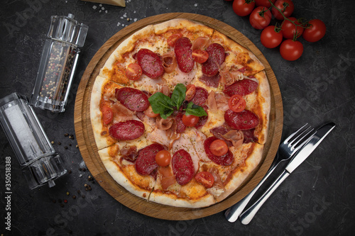 Italian pizza with tomatoes salami, parma, meat and cheese on a black background