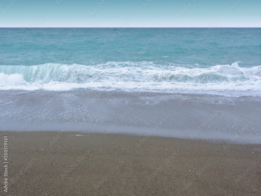 View of the blue stormy sea, white foam, waves, dark sand, empty coast.
