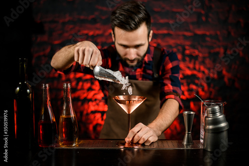 professional male bartender pours ice into metal martini glass