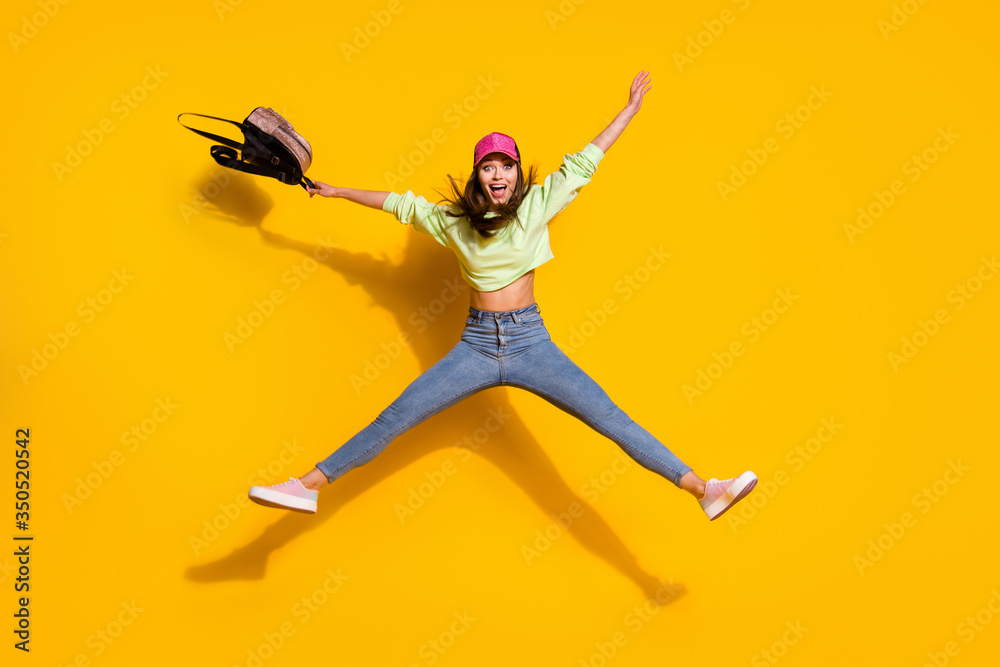 Full body photo of funky energetic lady college student hold backpack jump high up rejoicing wear green cropped sweatshirt jeans shoes cap isolated vivid bright yellow color background
