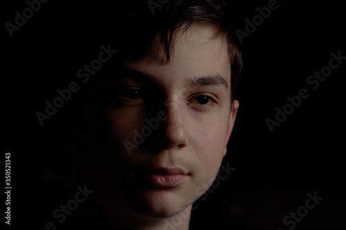 Portrait of a teenager on a black background. The boy has dark hair
