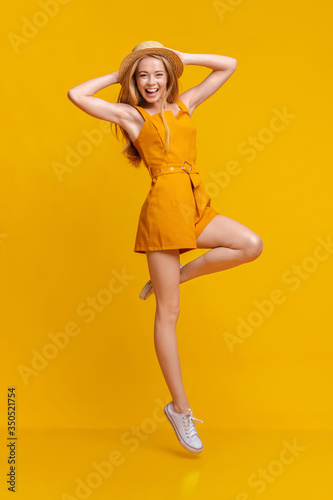 Summer Fashion. Joyful Girl In Jumpsuit And Hat Jumping On Yellow Background