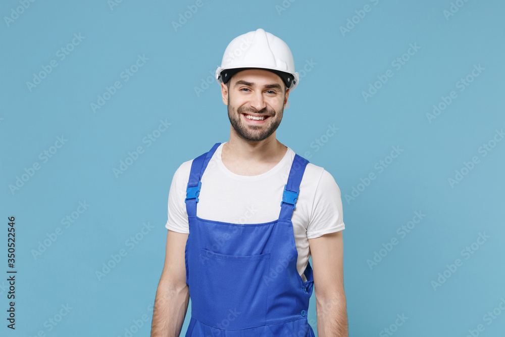 Smiling young man in coveralls protective helmet hardhat isolated on pastel blue background studio portrait. Instruments accessories for renovation apartment room. Repair home concept. Looking camera.