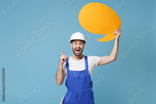 Excited man in coveralls helmet hardhat hold Say cloud isolated on blue background. Instruments accessories for renovation apartment room. Repair home concept. Pointing index finger up with new idea.